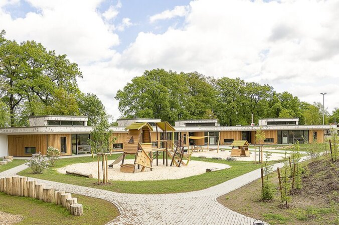 grande aire de jeux en bois sur une surface sablonneuse entre les bâtiments d'un jardin d'enfants