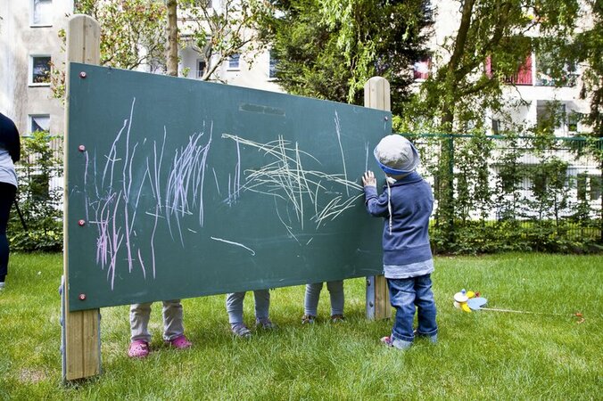 Toddler painting on large board on a green area.