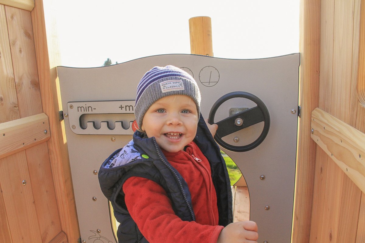 Playground equipment for childcare facilities from eibe - toddler laughing into the camera on a play tower.