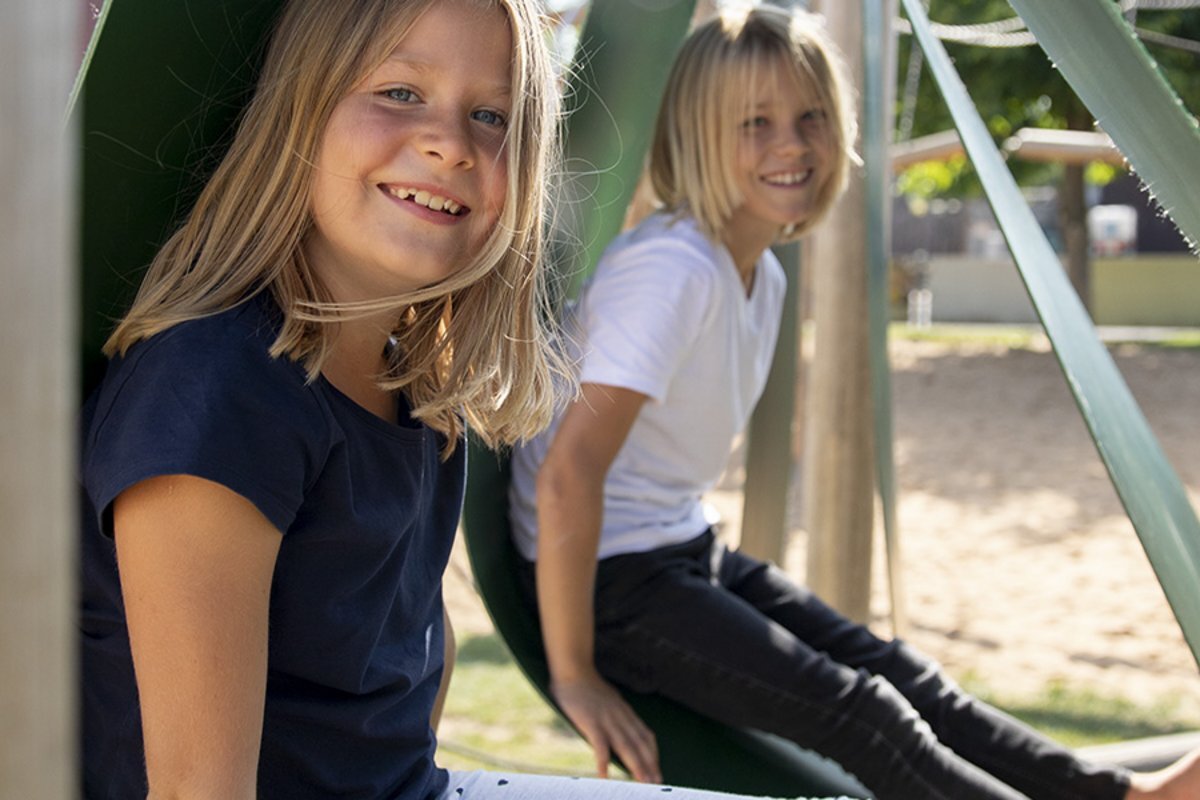 Deux filles souriantes assises dans des équipements de jeux eibe dans leur cour d'école